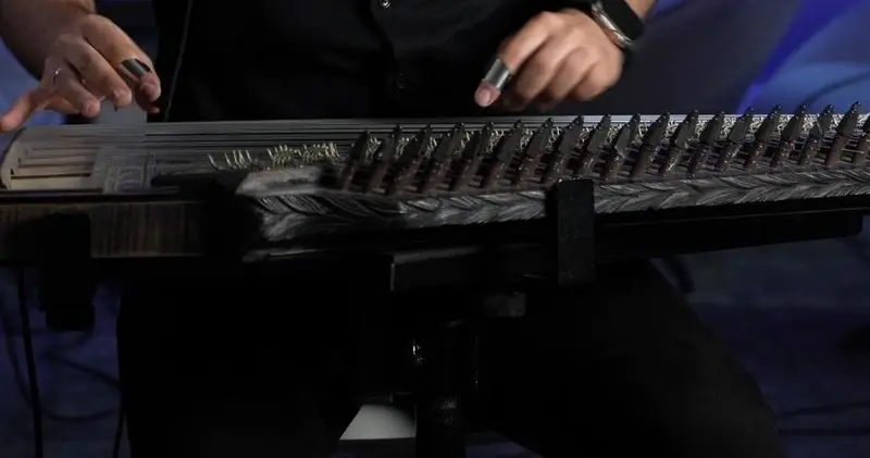 Close view of a qanun player's hands plucking the strings with finger picks