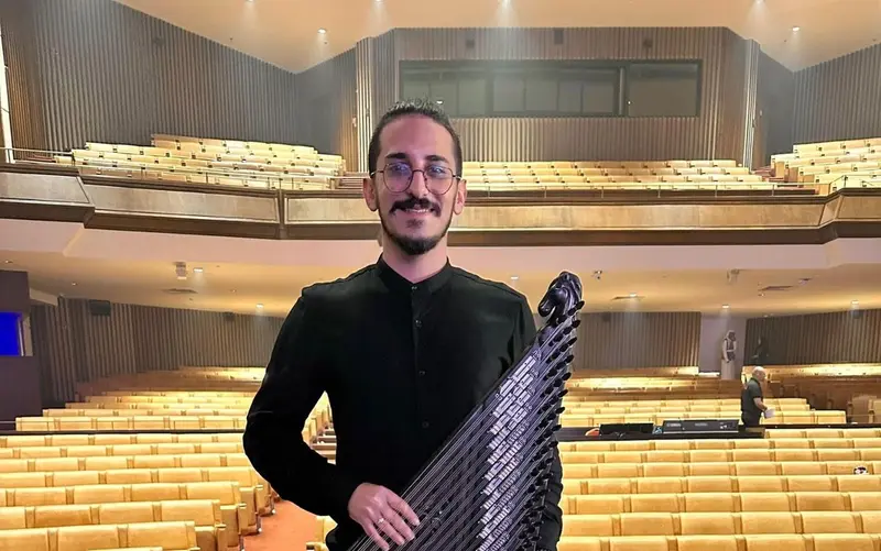 Qanun player holding his qanun upright in an empty concert hall before a performance