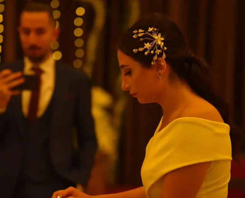 Qanun player in a yellow dress plucking the strings at an evening event while a guest films